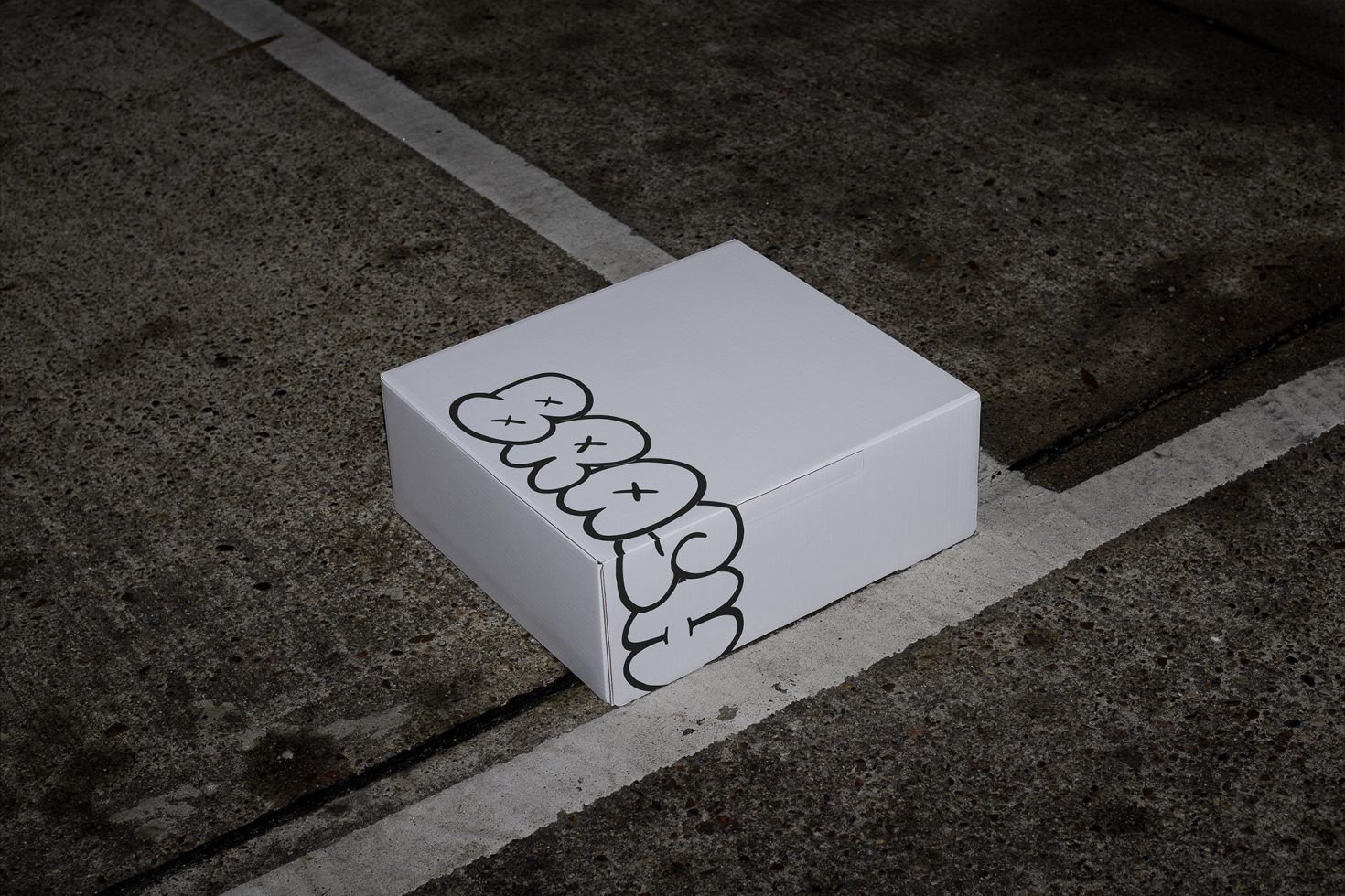 White blank box mockup with black artistic design on dark urban concrete floor, packaging design presentation, realistic product mockup.